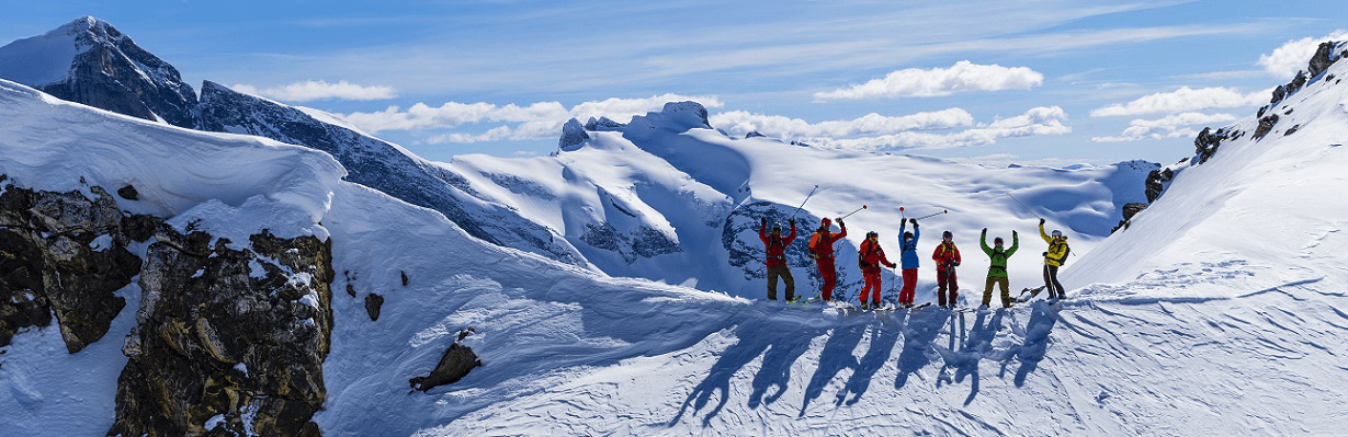 Heliski group waving from mountain ridge top.